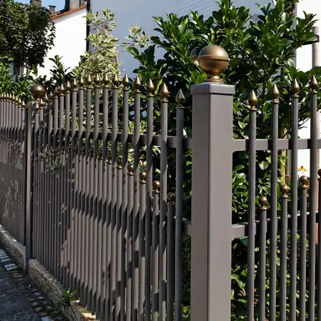 Stabmattenzaun aus Metall mit goldenen Zierspitzen vor dichtem grünen Garten.