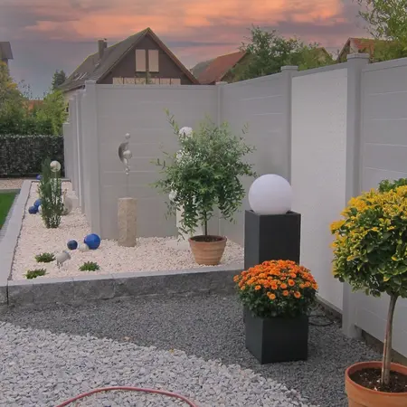 Moderner Garten mit Sichtschutzzaun, Kies, Zierpflanzen und dekorativer Beleuchtung.