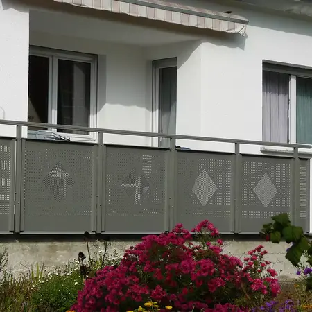 Moderner Balkon mit grauem Metallgeländer und Lochmuster vor weißer Hausfassade.