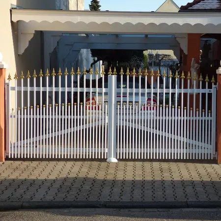 Weißes Einfahrtstor aus Metall mit goldenen Spitzen vor einem überdachten Carport.