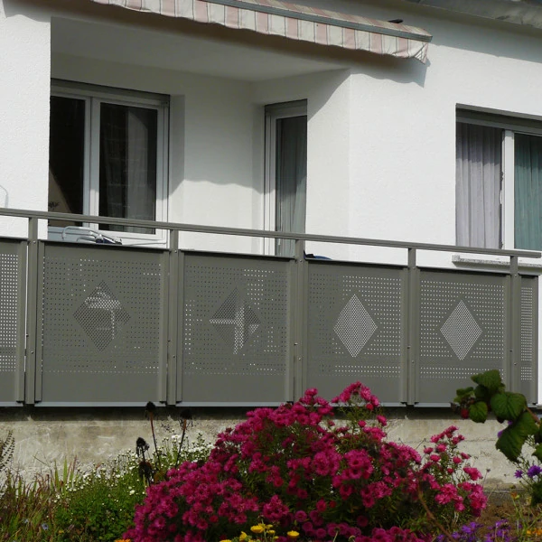 Moderner Balkon mit grauem Metallgeländer und floralem Vorgarten vor weißem Haus.