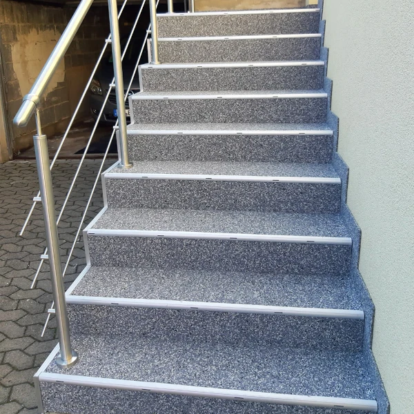 Außentreppe mit Granit-Belag und Edelstahlgeländer vor einem modernen Gebäude.