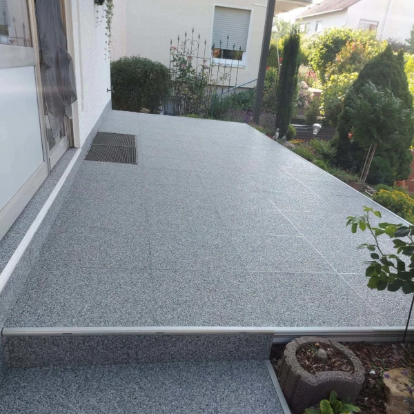 Moderne Terrasse mit grauen Fliesen und Stufen, umgeben von gepflegtem Garten.